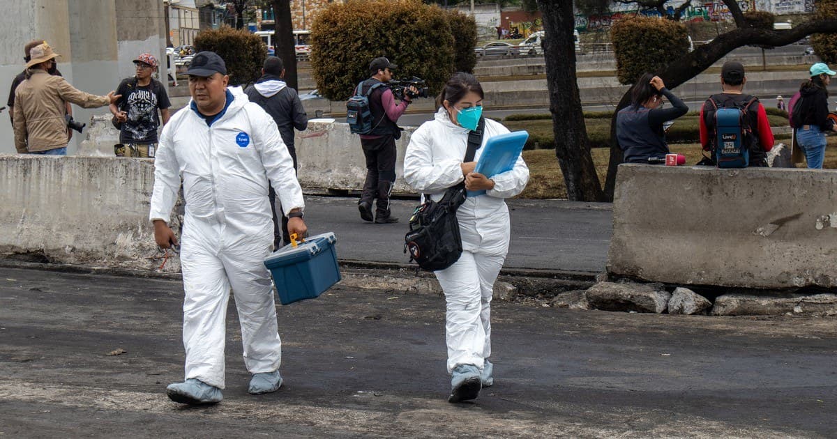 Peritos de la Fiscalía de la Ciudad de México con trajes blancos de protección cruzan el asfalto quemado junto a los muros de contención del Puente de la Concordia, un día después de la explosión.