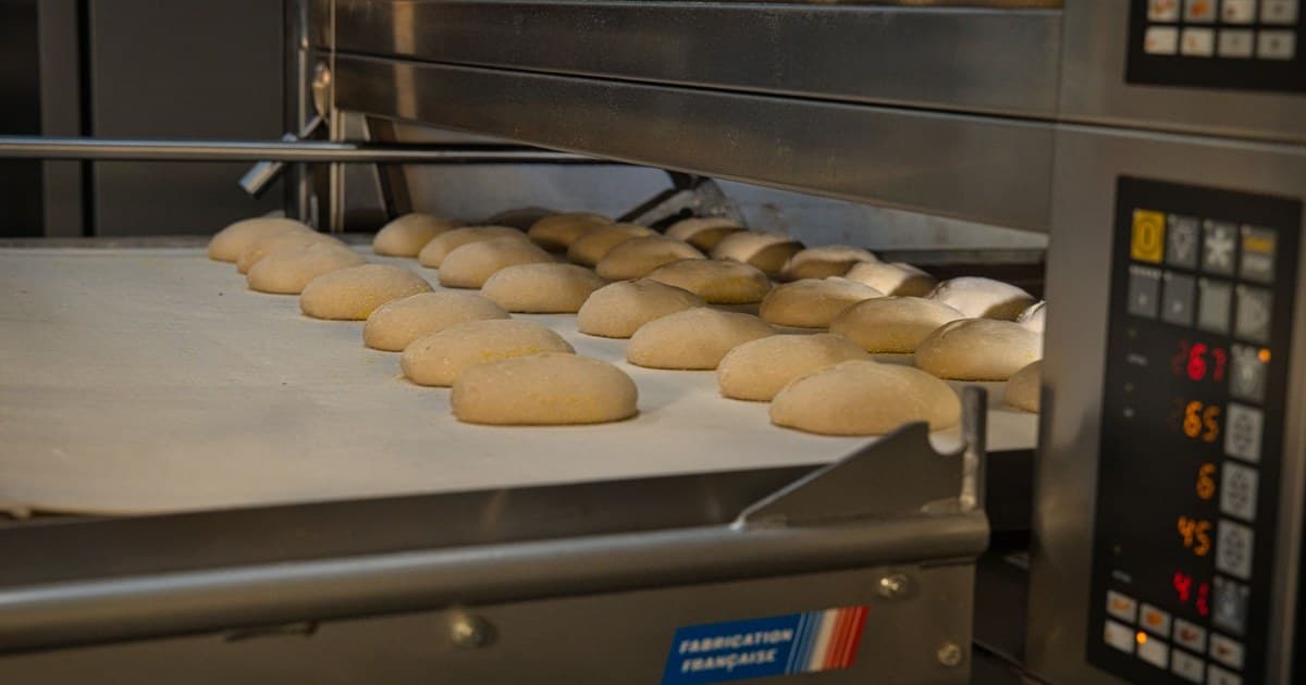 Charola de masa entrando a un horno industrial de panadería con su panel de control encendido.